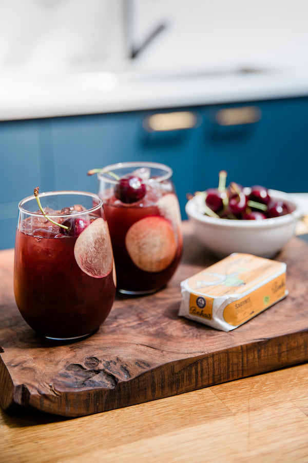Close-up of a wooden platter that holds two glasses of non-alcoholic cocktails and a bowl of cherries.