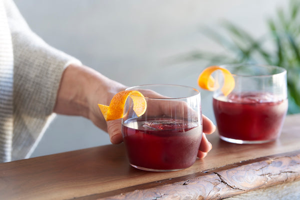 Close-up of two short glasses of a cherry-red non-alcoholic cocktail with orange peel garnishes.