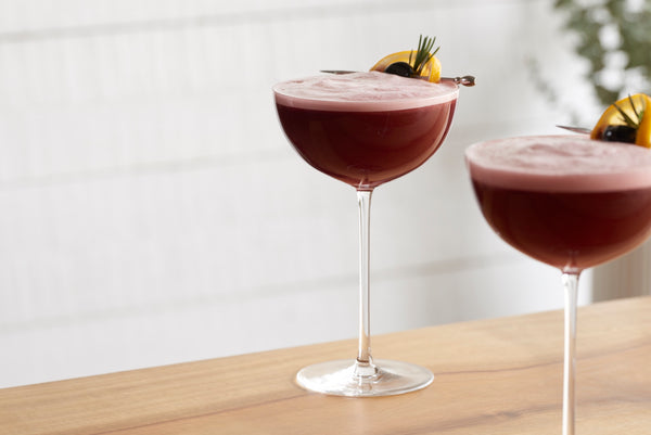 Close-up of two martini glasses containing cherry-red non-alcoholic mixed drinks with cherry and lemon garnishes.
