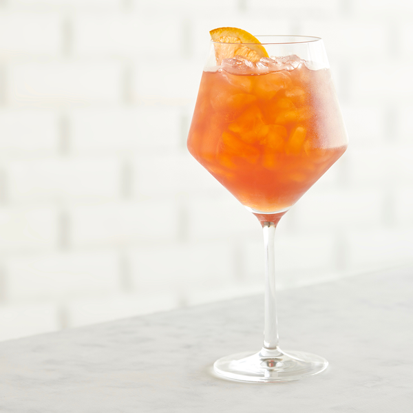 Close-up of a wine glass containing an orange non-alcoholic cocktail with an orange wedge garnish.